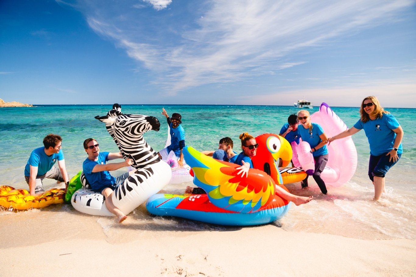 Group on big pool inflatables on the beach with clear blue sea behind